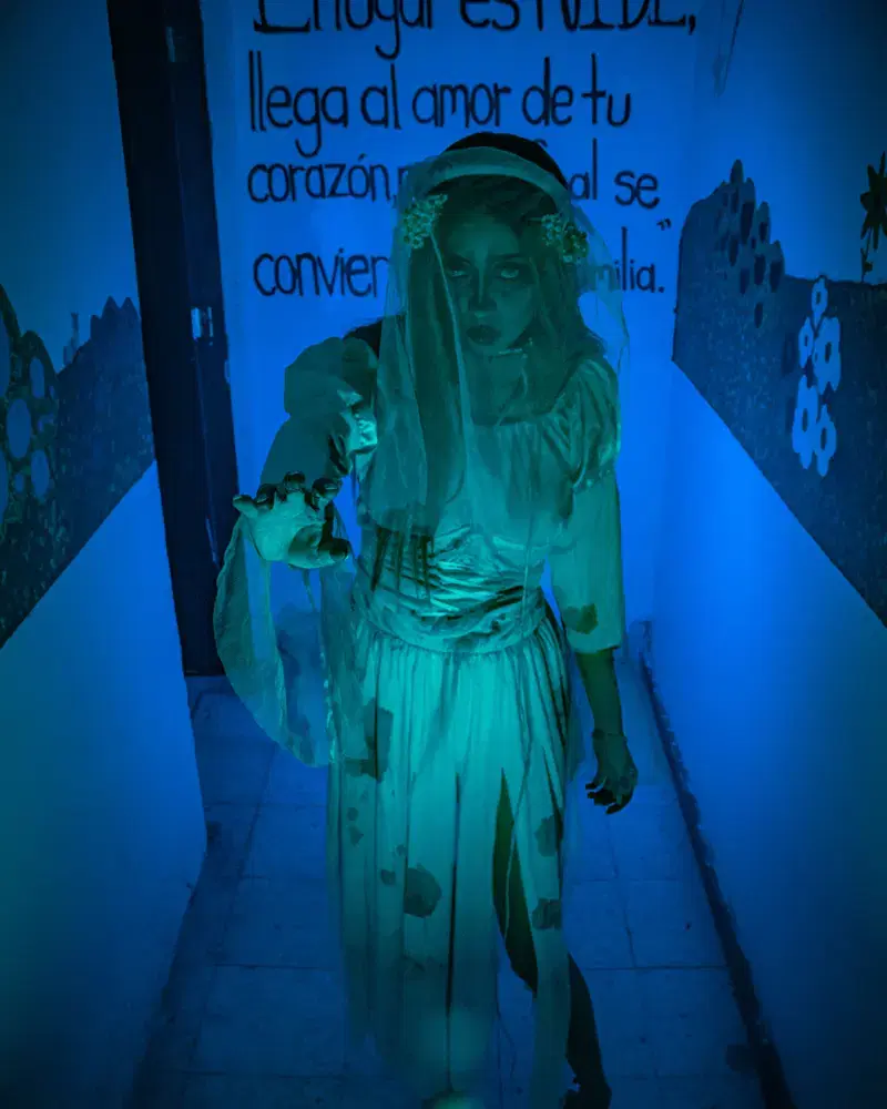 Invitada vestida de blanco iluminada con luz negra en un pasillo azul
