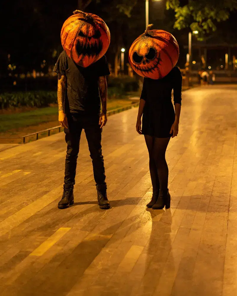 Dos invitados con cabezas de calabaza hechas a mano caminando de noche