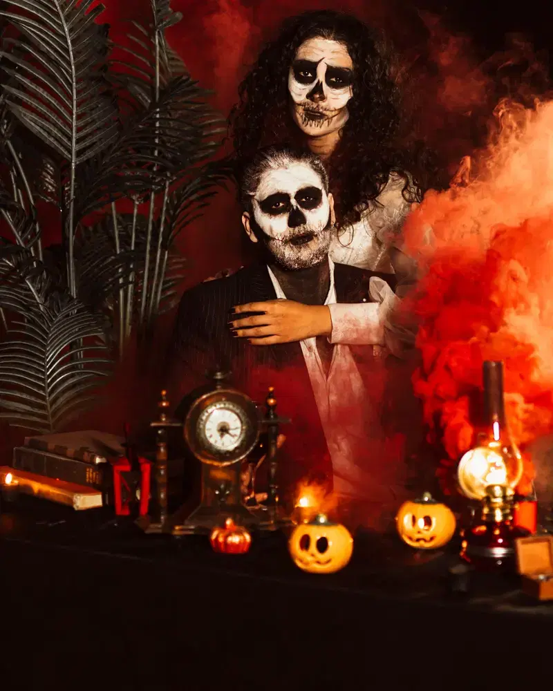 Pareja con maquillaje de calavera entre humo rojo y velas en una fiesta de disfraces